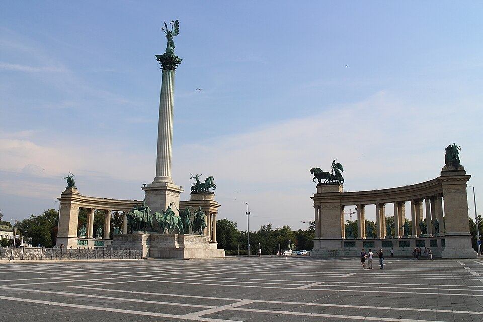 Wide view of Heroes' Square in Budapest with the Millennium Monument column, the Archangel Gabriel statue on top, and the curved colonnades of Hungarian leaders on either side