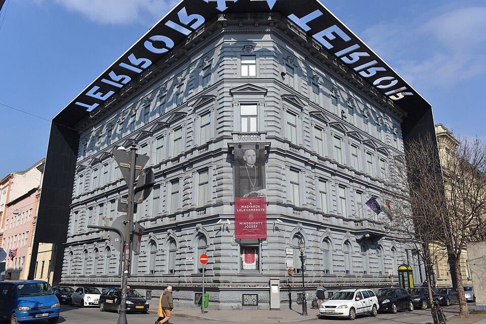 Grey stone facade of the House of Terror museum building on Andrassy ut, Budapest, with its iconic overhanging black cornice cut out with the word TERROR casting a shadow onto the wall