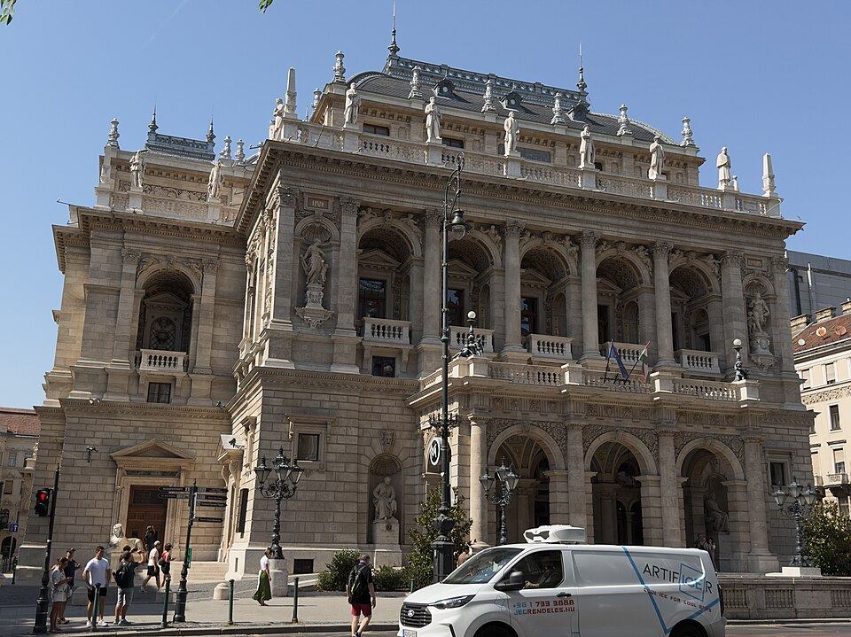 Neo-Renaissance facade of the Hungarian State Opera House in Budapest, with statues along the roofline and arched windows, viewed from the street